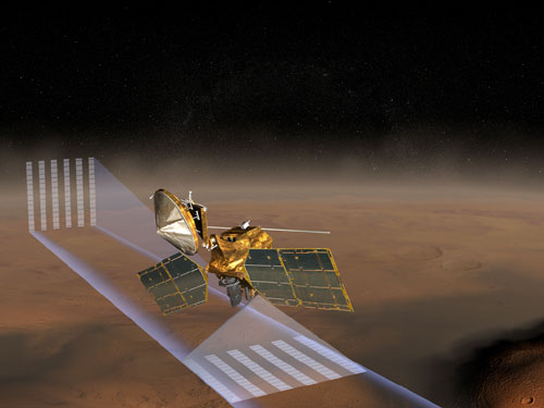 In this artist's concept image, the Mars Reconnaissance Orbiter orbits above the orange-red surface of Mars.  The planet's thin atmosphere is represented by a whitish haze above the surface.  The spacecraft is using its Mars Climate Sounder instrument to take vertical profiles of the atmosphere, represented by tall, thin, bluish-white beams that are scored like lined notebook paper.