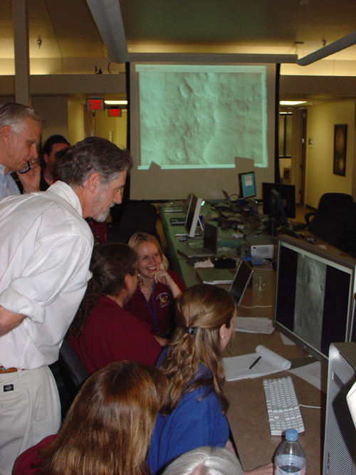 In this photo, several HiRISE team members hover around a computer screen looking at the first image from HiRISE.
