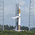 This image is a view of Launch Complex 41 at Cape Canaveral Air Force Station in Florida.  The large Atlas V rocket that will carry the Mars Reconnaissance Orbiter through Earth's atmosphere sits tall and majestic against a light blue sky blotted with very faint white clouds.  The lower stage of the rocket (closest to the ground) is half copper-colored and half white.  The upper stage, which is roughly half the size of the lower stage, is white and gold.  White smoke billows from the adaptor area where the stages meet as the 'wet dress rehearsal' is conducted.  To the left and right of the rocket sit two large towers that serve as lightning rods to protect the rocket and spacecraft from strikes.
