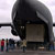 In this image, more than a dozen people stand, in winter coats, behind a huge, gray military C-17 cargo plane.  From this vantage point, the plane resembles a huge shark with its mouth wide open.  Inside the 'mouth' is one of the large boxes that contain the Mars Reconnaissance Orbiter.  The wings of the plane jut out from both sides.  The sky is cloud-covered.