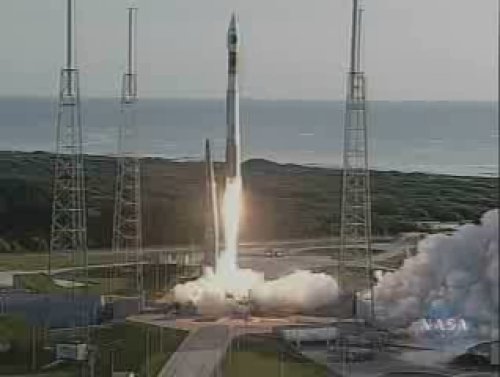n this image, the enormous Atlas V rocket lifts off of the launch pad, carrying the Mars Reconnaissance Orbiter through Earth's atmosphere and putting on its trajectory toward Mars. Fire spits out of the rocket and clouds of smoke surround it. The Atlantic Ocean is in the background.