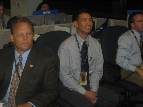 This photo shows three men in business suits, smiling at the launch that they are watching on TV screens that are out of this picture.  Kyle Martin is a strong man with blond hair, and he is looking at the screen as if he's willing the rocket to succeed!  Peter Xaypraseuth is a young Asian man with a big, excited smile, and he sits on the edge of his seat with his hands clasped between his legs.  David Skulsky is a young man with dark hair and sideburns, and he wears glasses.  David's mouth is slightly open in anticipation or awe.