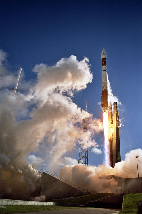 This image features a view from below an Atlas 5 rocket as it lifts off. A bright blue sky is filled with clouds of smoke from the launch.