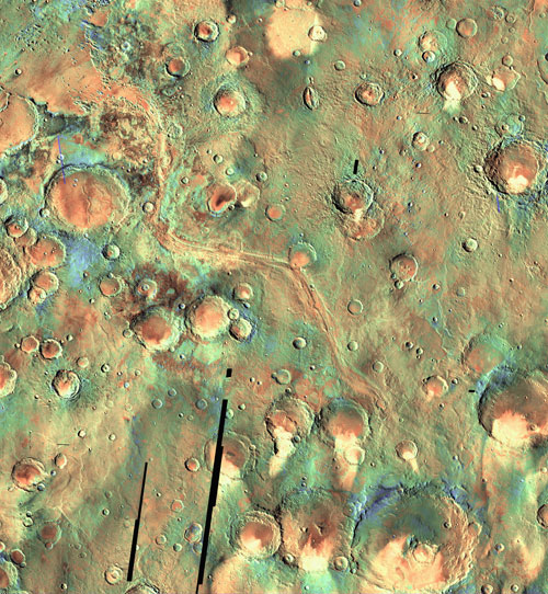 This color image shows an overhead view of a meandering channel winding from the lower right edge toward the upper left edge. On either side of the channel are a variety of craters. Near the top, where the channel opens out onto a flatter area, is a crater that is somewhat larger than the others. The bed of the channel and the crater interiors are reddish in color. The reatively flat surface north and south of the large crater is light blue.