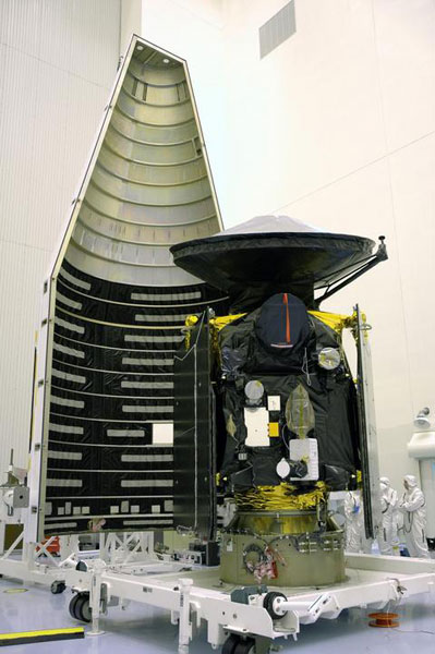 This image features the large Mars Reconnaissance Orbiter spacecraft being loaded into its protective fairing in the very white cleanroom of the Payload Hazardous Servicing Facility.  The fairing is open and appears 