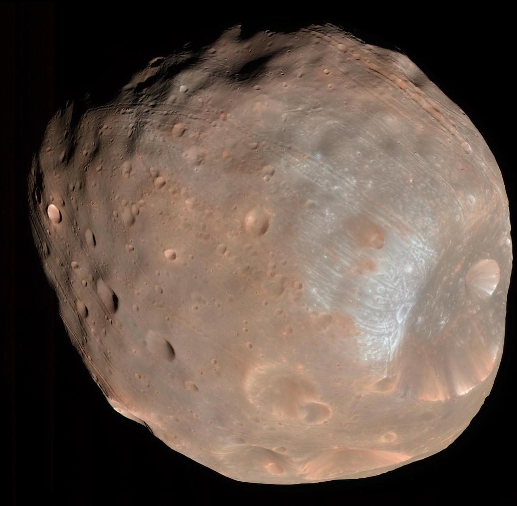 This is a color image of the largest of Mars' two moons, Phobos. It appears pinkish in color with a giant crater dent on the far, right-side. The crater edges seem whiter than the rest of the image.