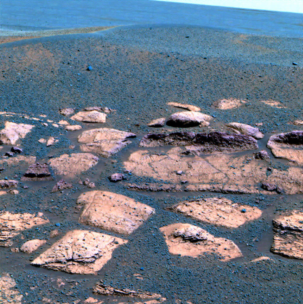 This false color image suggests that the plains beyond the small crater where the Mars Exploration Rover Opportunity now sits are littered with the same dark grey material found inside the crater in the form of spherules or "blueberries."