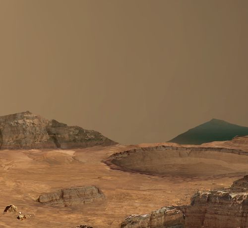 This image shows a round crater exposing horizontal layers in its walls. Around it is an undulating brown surface. In both the foreground, in the lower right corner of the image, and in the backround, forming the horizon, are cliffs exposing horizontal layers of rock. The sky is a typical shade of martian peachy pink.