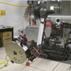 In this video clip, the camera swerves around the room where testing is underway for Curiosity's robotic arm.  The camera zooms in on the robotic arm as the arm moves up from the stowed position and then rotates a set of tools at the end of the arm.  A JPL engineer is crouched down behind the arm in the background and gives a thumbs-up once the tools stop rotating.